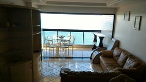 Un salon avec vue sur la mer, un coin repas avec des chaises et une table, et un canapé en cuir.