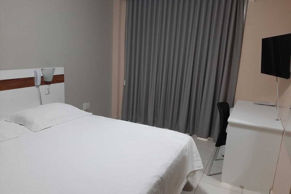 A hotel room with a bed, a desk, a chair, a television, and a window with curtains.