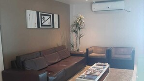 Un salon avec un canapé en cuir marron, une table basse blanche, un tapis gris et une plante en pot.