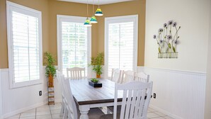 Uma sala de jantar com mesa de madeira, cadeiras brancas e plantas em vasos.