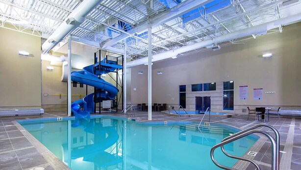Une piscine intérieure dotée d’un toboggan bleu, d’un plafond haut avec des poutres apparentes et d’un sol carrelé.