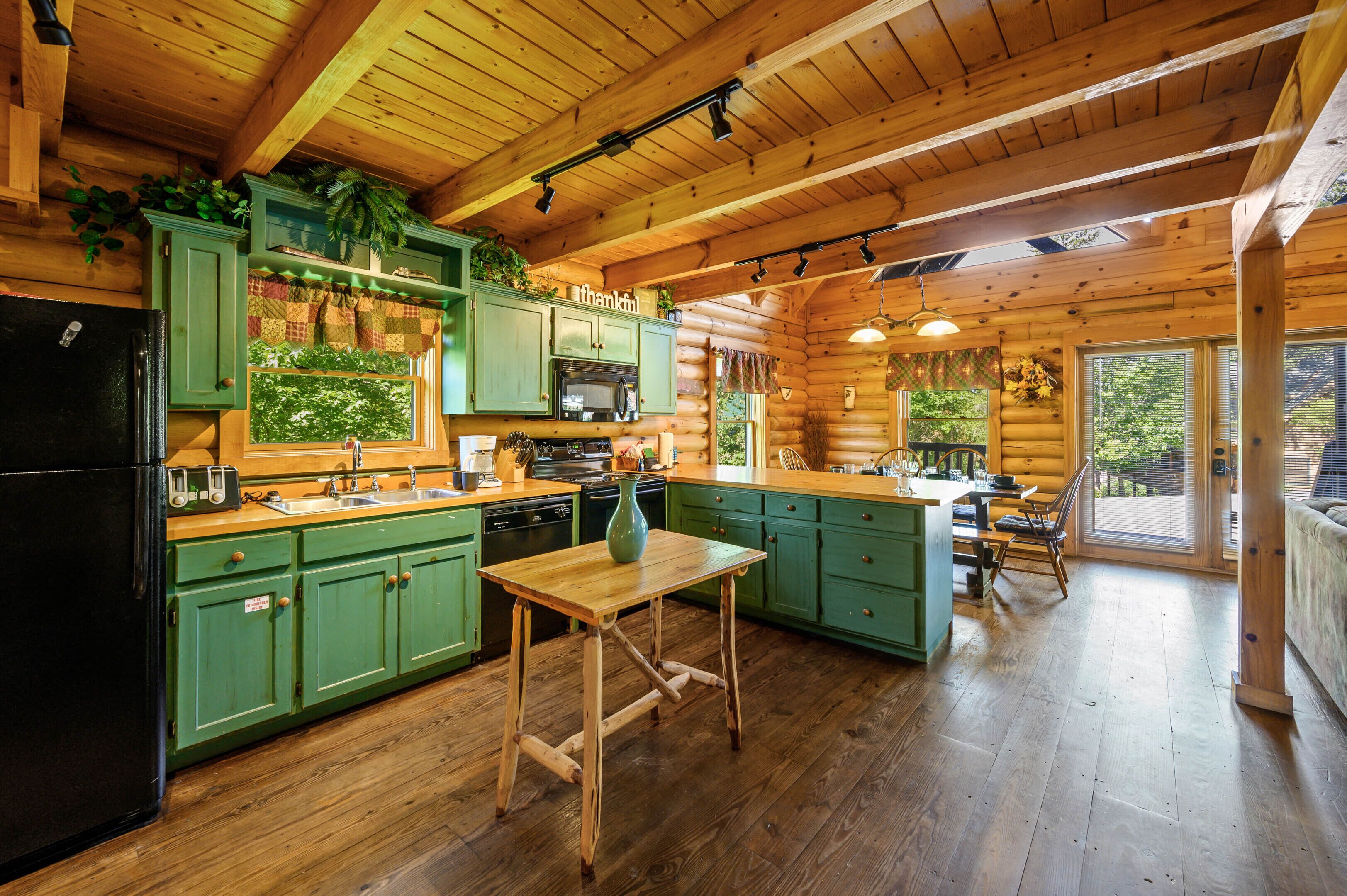 A log cabin kitchen with green cabinets, wooden countertops, a black refrigerator, a wooden dining table, and a large window.
