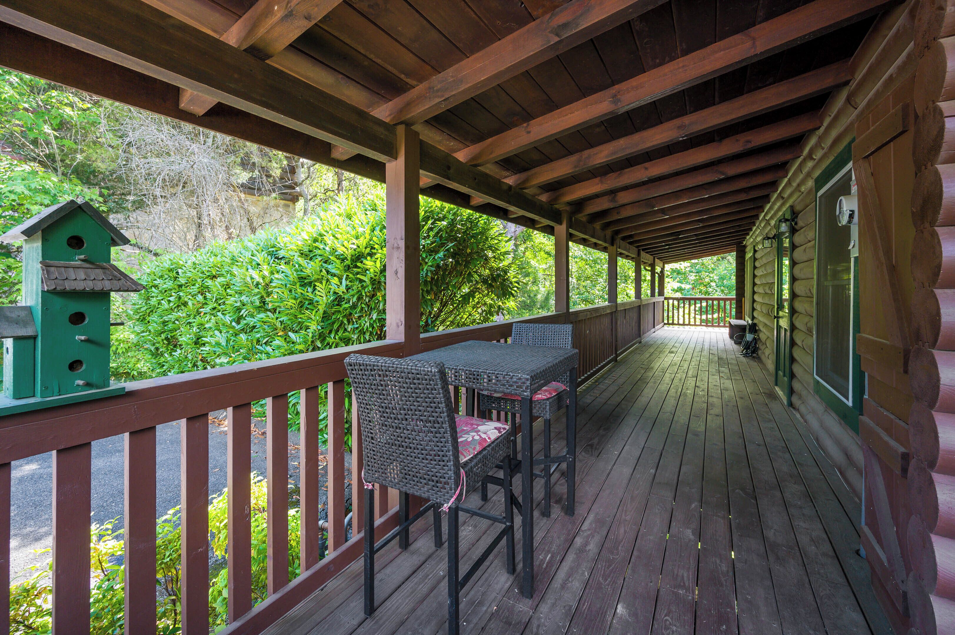 A wooden deck with a table and chairs, surrounded by lush greenery.
