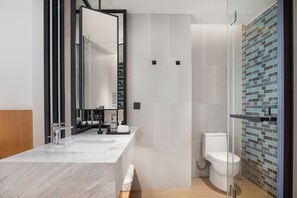 A modern bathroom with a marble sink, a large mirror, a toilet, and a shower area with a tiled wall.