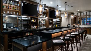 A bar area with a long counter, stools, and shelves stocked with bottles and glasses.