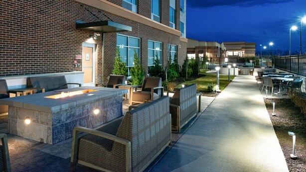 An outdoor patio area with seating and a fire feature, adjacent to a building with large windows and a brick facade.