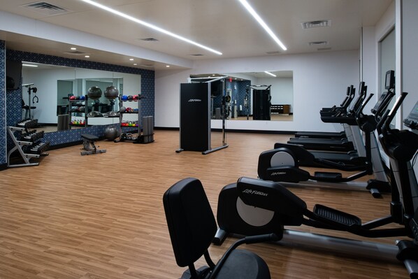 Un gimnasio con equipo de cardio, máquinas de pesas y un espejo grande.