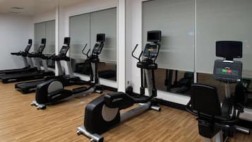 A row of stationary bikes in a gym with wooden flooring and large windows.