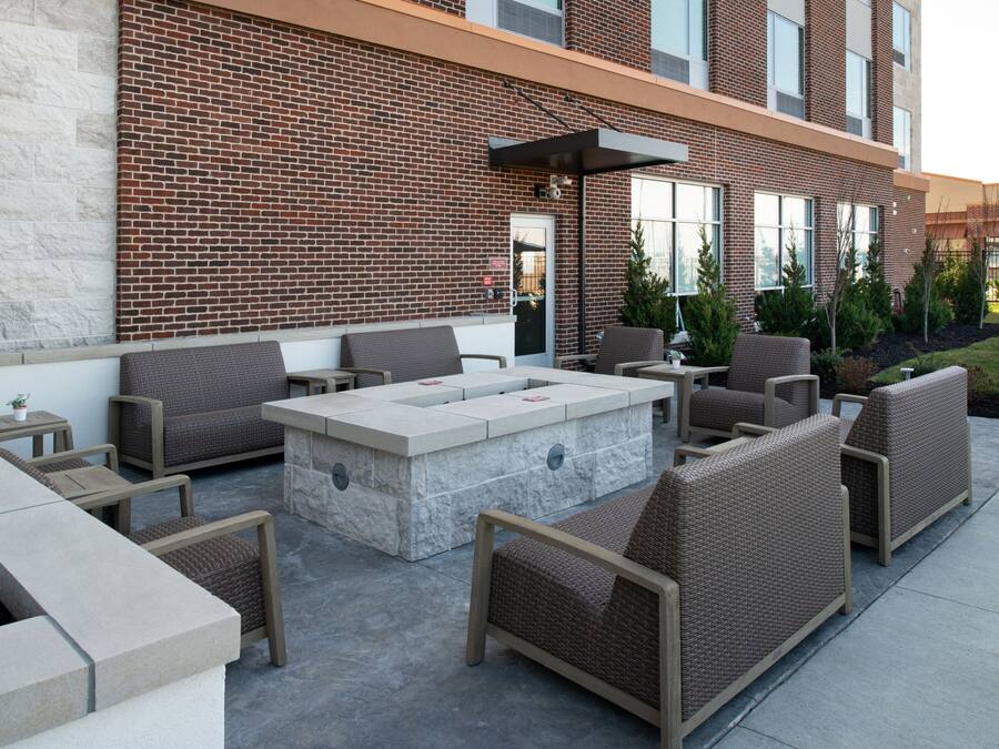 Un patio al aire libre con mobiliario de mimbre, una chimenea de piedra y un edificio de ladrillo al fondo.