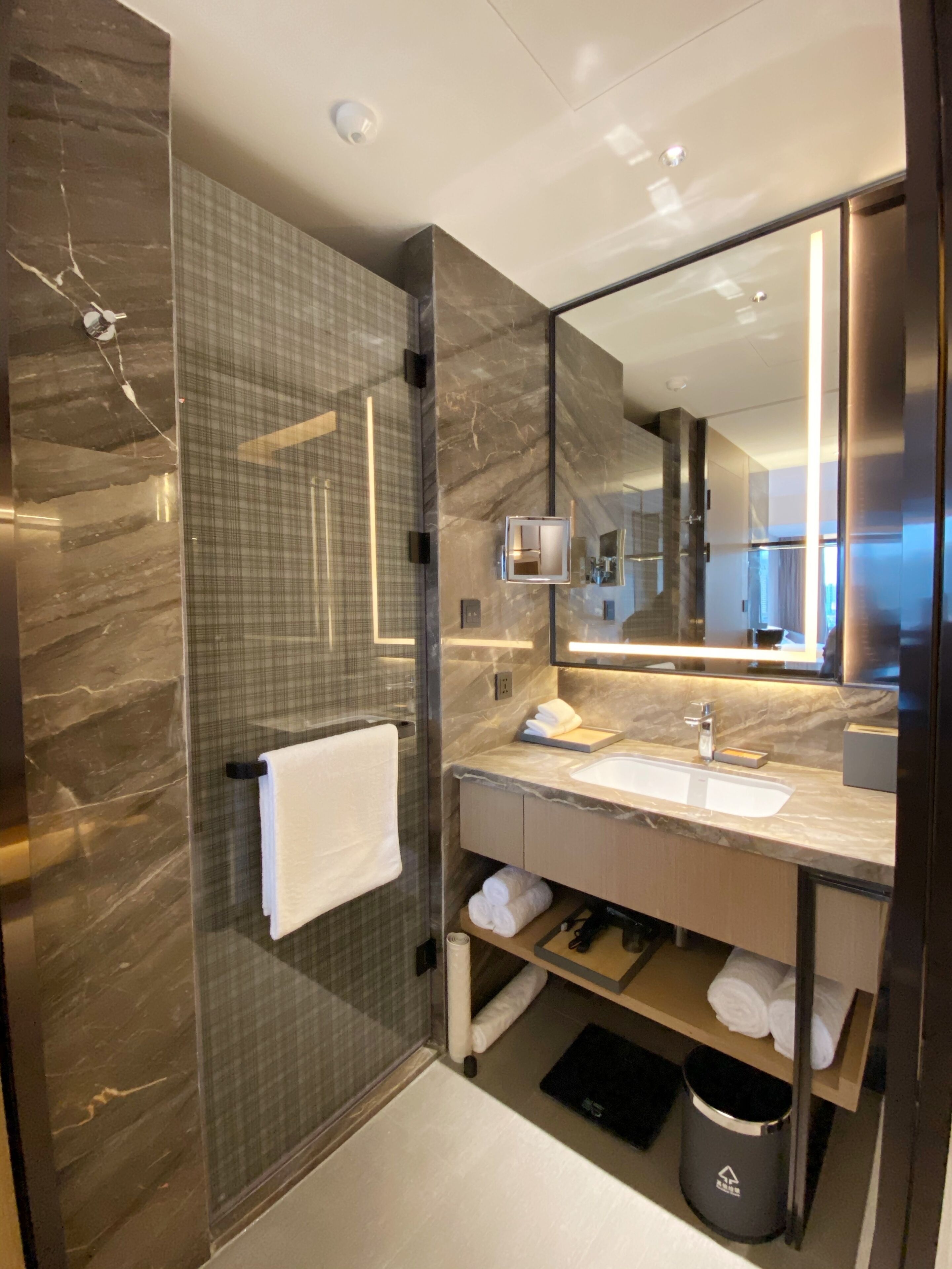 A modern bathroom with a glass-enclosed shower, a large mirror, a marble countertop, and a built-in sink.