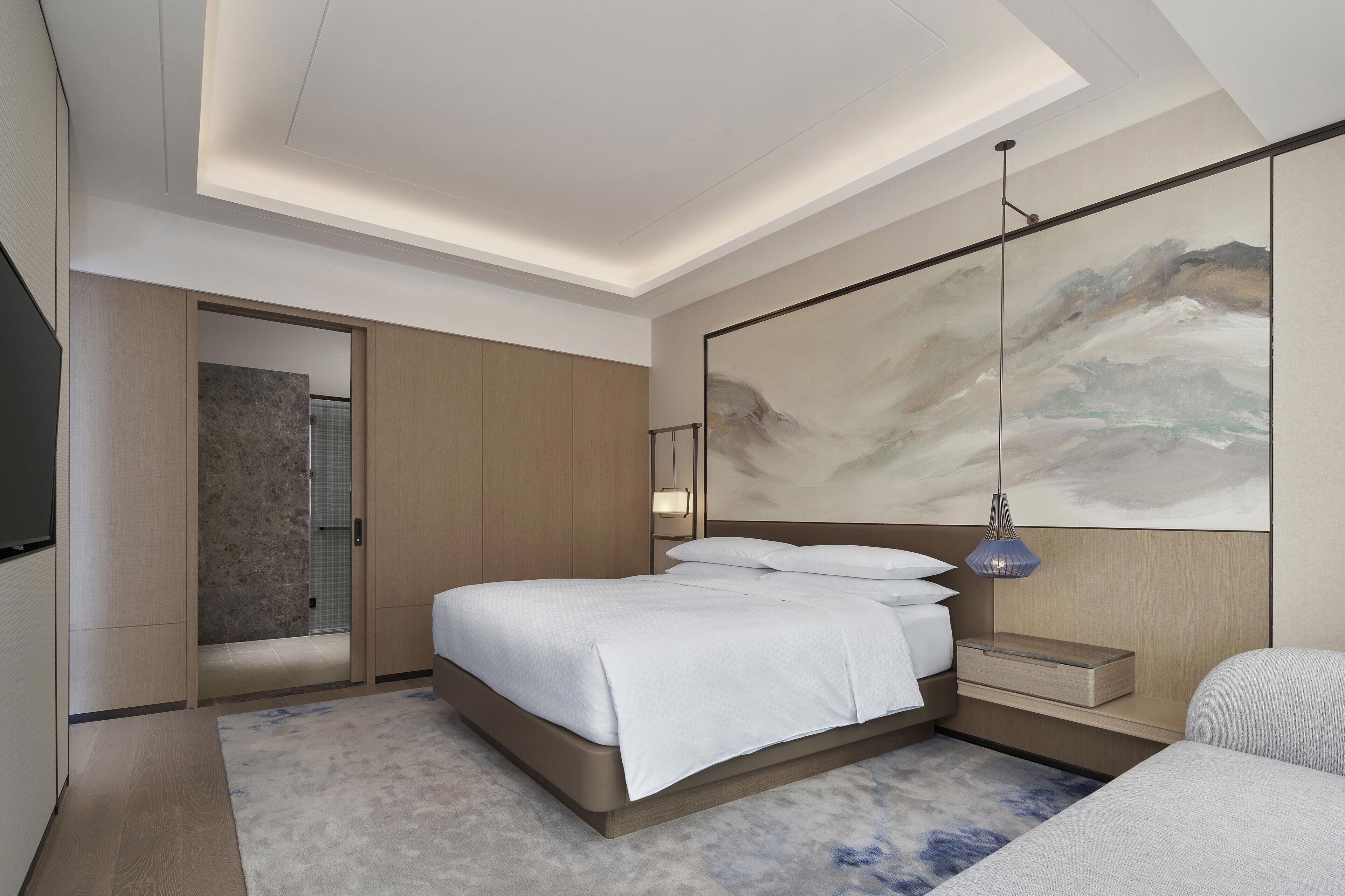 A modern hotel room with a large bed, a bedside table, a mounted artwork, and a shower area.