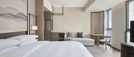 Habitación de hotel moderna con una cama grande, un escritorio, una silla y vistas de la ciudad a través de amplios ventanales.