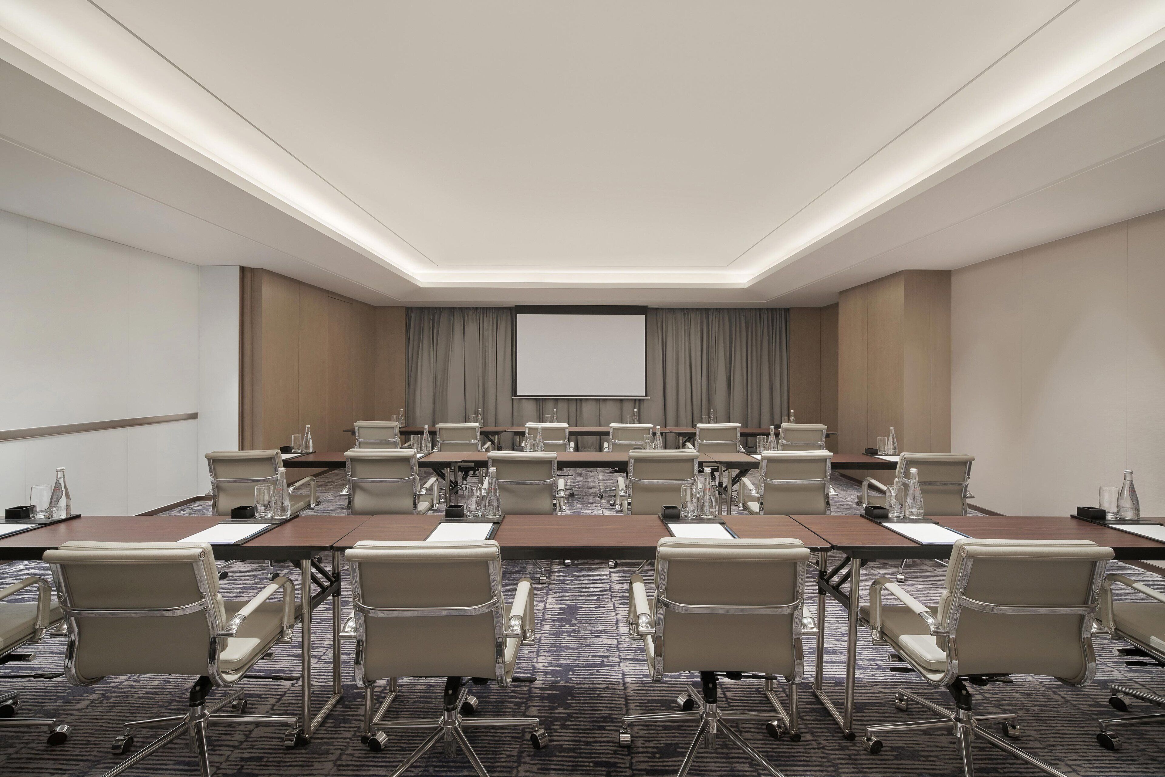 A conference room with a large screen, multiple tables, and chairs arranged for meetings.