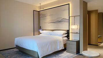 A modern hotel room with a large bed, bedside tables, a small round table, and a wall-mounted artwork.