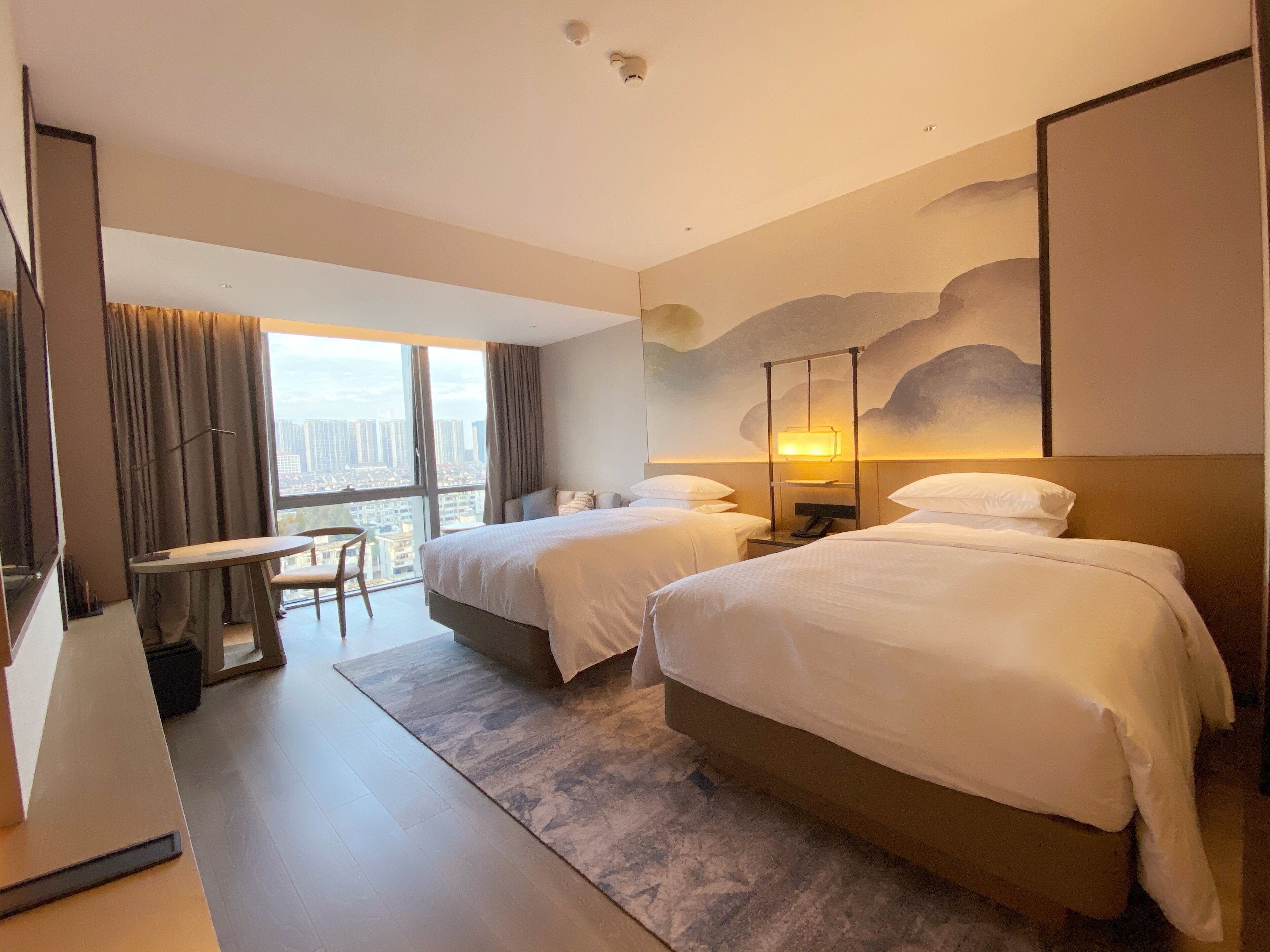 Een hotelkamer met twee bedden, een bureau en uitzicht op de stad.