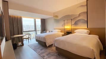 Habitación de hotel con dos camas, un escritorio y vistas a la ciudad.