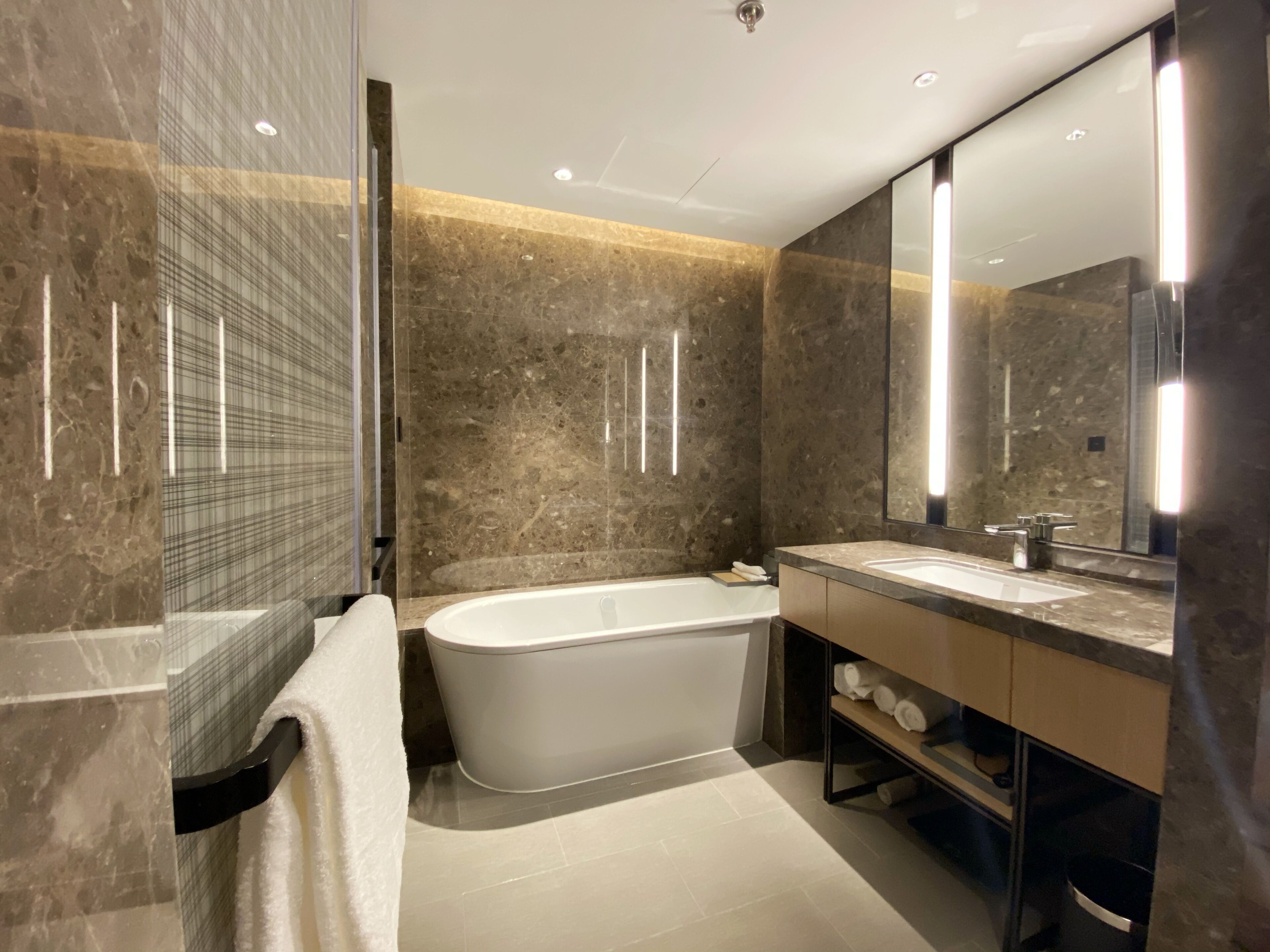 A modern bathroom with a freestanding bathtub, a large mirror, and marble walls.