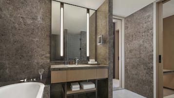 A modern bathroom with a marble wall, a large mirror, a bathtub, and a wooden vanity.