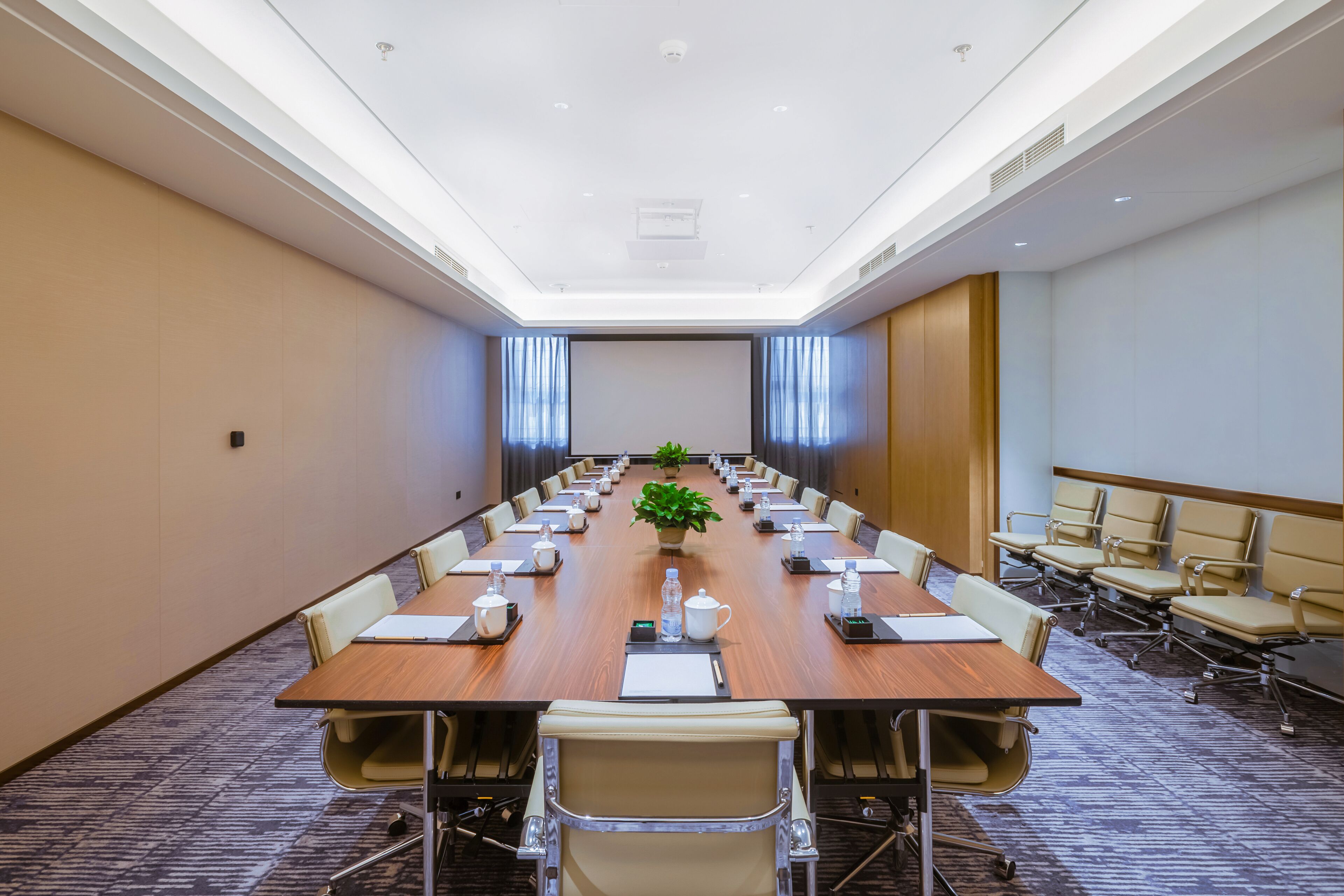 A conference room with a long table, chairs, a projector screen, and a plant.