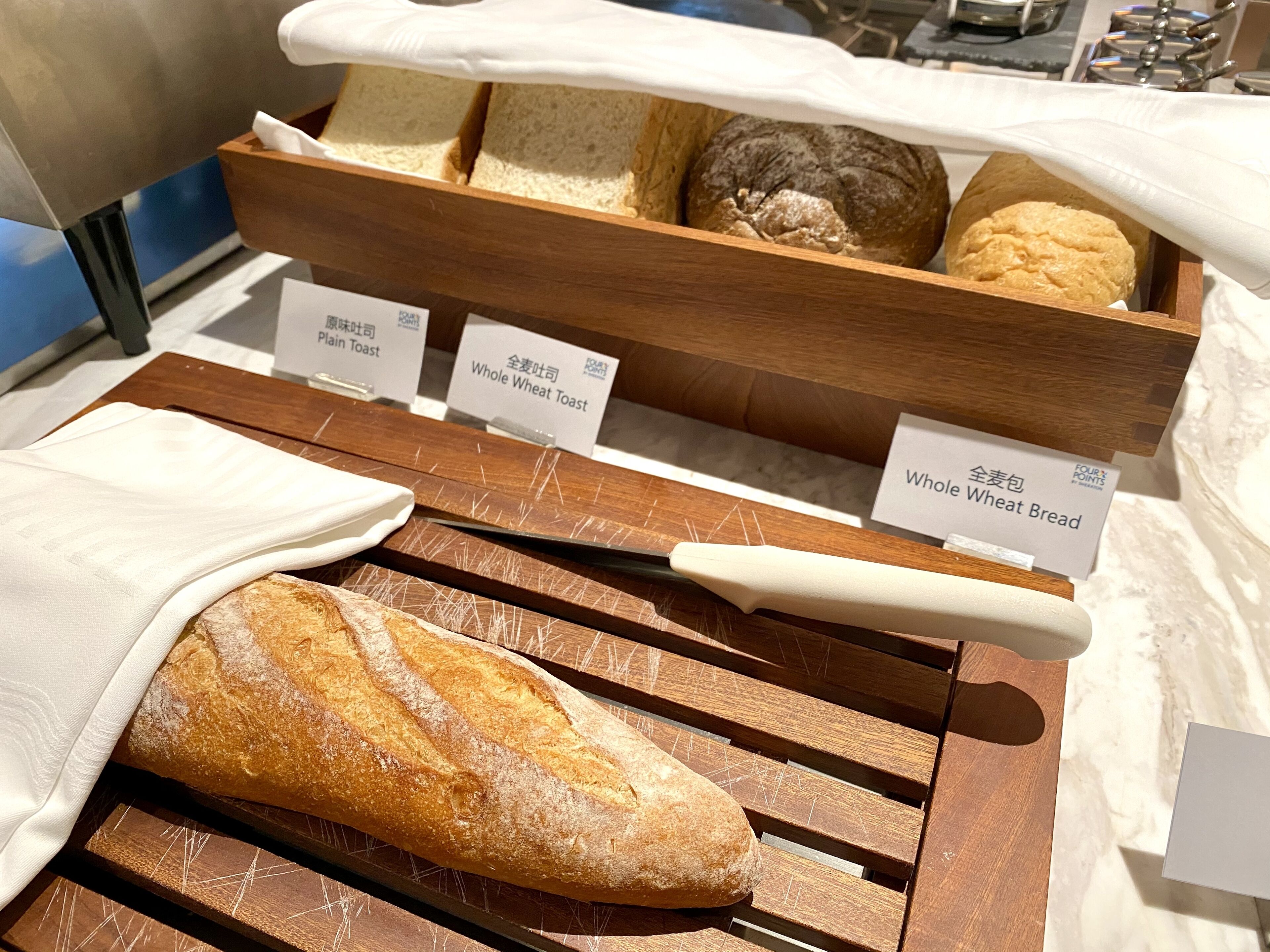 Une sélection de pains, présentés sur une planche en bois, avec des étiquettes indiquant les différents types, comme « pain de mie nature » et « pain complet ».