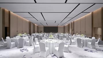 Un amplio salón de banquetes con mesas redondas y sillas blancas, una pantalla grande al frente y suelo alfombrado.