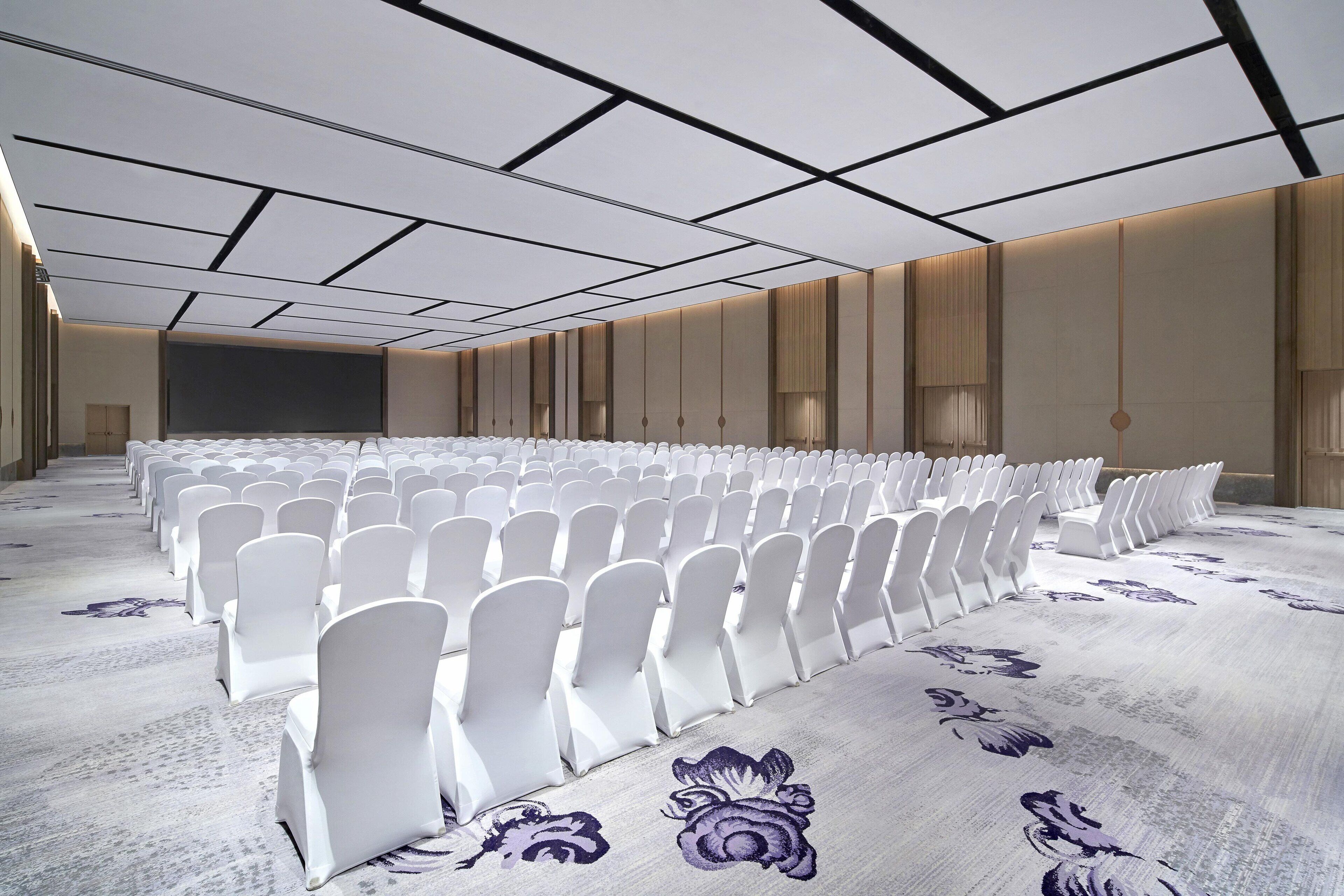 A conference room with rows of white chairs, a large screen, and patterned carpet.