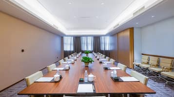 Un salón de conferencias con una larga mesa, sillas y una planta en maceta.