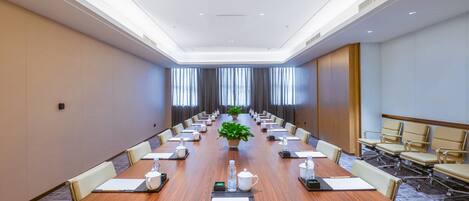 Un salón de conferencias con una larga mesa, sillas y una planta en maceta.