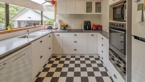 A compact kitchen with white cabinets, a black and white checkered floor, and a view of the outdoors through a window. - Duvauchelle Dream (Duvauchelle)