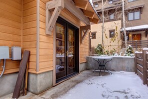 Un edificio de madera con puerta de vidrio, una mesa de hormigón y un banco de metal en el exterior.