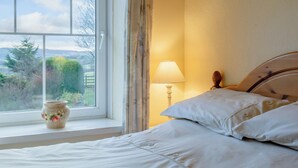 A bedroom with a bed, a window with a view of greenery, a lamp, and a vase on the windowsill. - 3 bedroom accommodation in Llanafan Fawr, near Builth Wells (Llanafan Fawr, near Builth Wells)