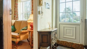 A cozy living room with a sofa, a table with a lamp, a wooden cabinet, and a large window with a view of trees. - 3 bedroom accommodation in Llanafan Fawr, near Builth Wells (Llanafan Fawr, near Builth Wells)