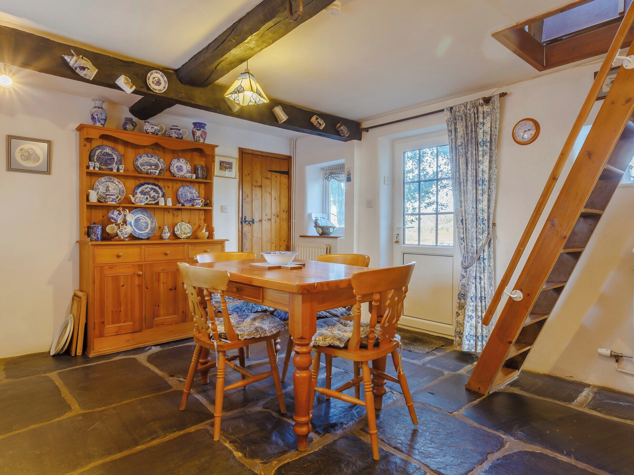 Ein Essbereich mit Holztisch und Stühlen, einem eingebauten Regal mit blau-weißen Tellern und einer Treppe, die zu einer oberen Ebene führt.