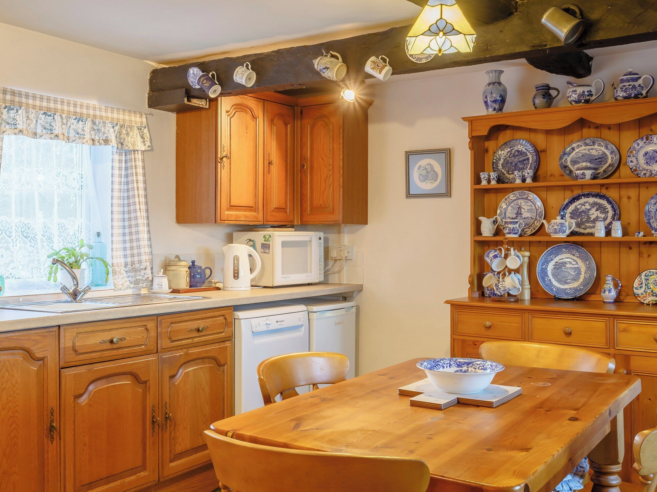 Een keuken met houten kastjes, een magnetron, een spoelbak en een eettafel met stoelen.