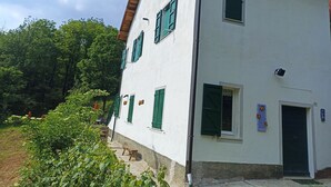 Un edificio blanco con contraventanas verdes, una escalera de madera y un pequeño jardín.