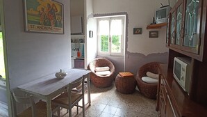 Una habitación acogedora con una mesa de comedor, dos sillas de mimbre, un televisor y una ventana que da a zonas verdes.
