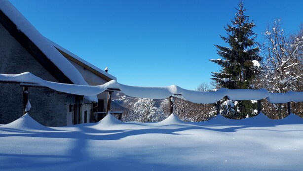 Un edificio cubierto de nieve con techo inclinado y cerca de madera.
