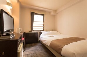 A hotel room with a bed, a desk with a television, a window with curtains, and a radiator.