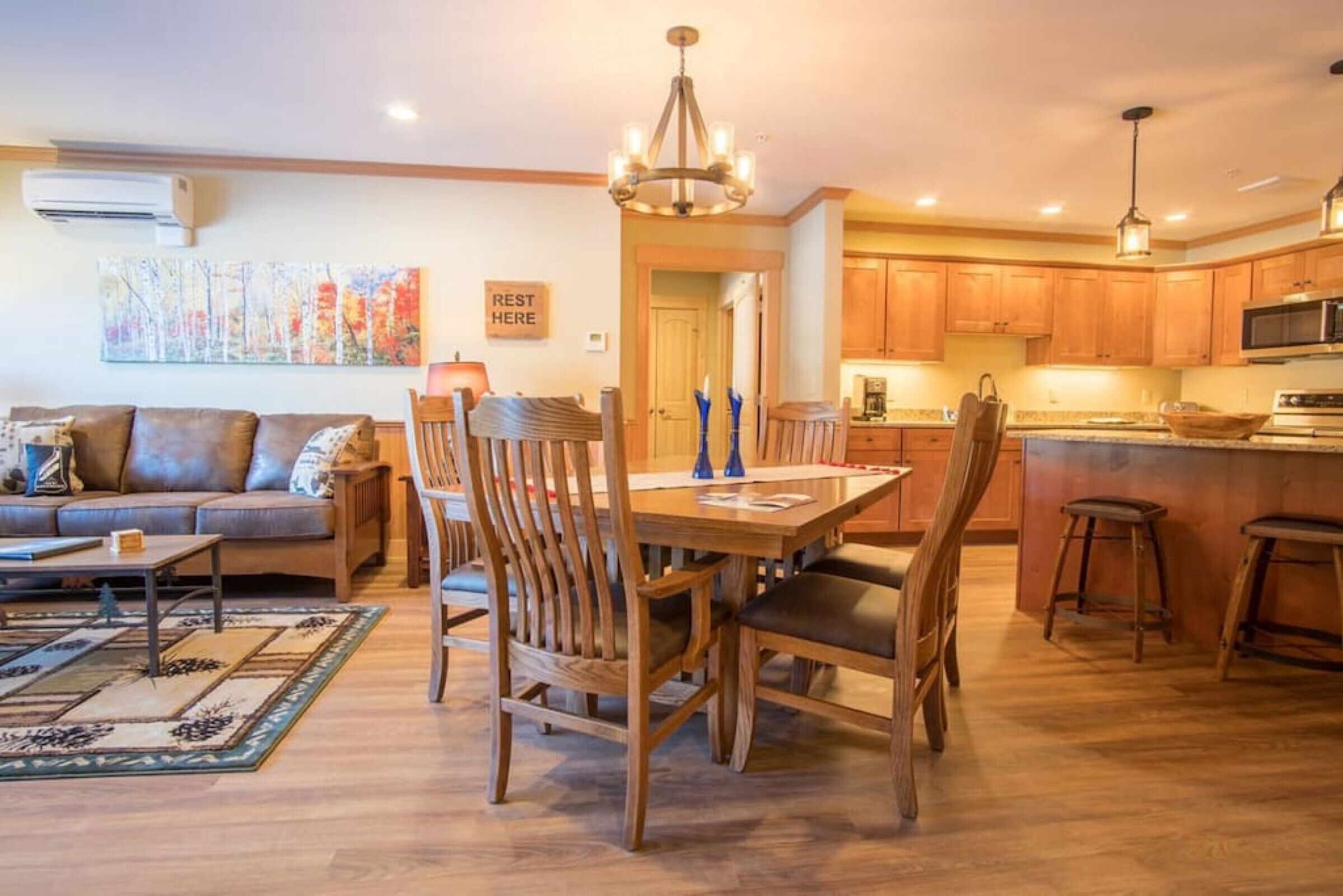 A spacious living room with a sofa, a dining table with chairs, and a kitchen area with wooden cabinets and a microwave.