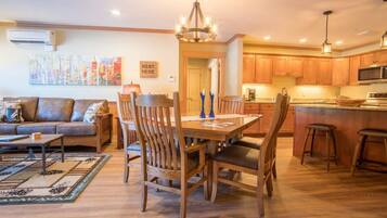 A spacious living room with a sofa, a dining table with chairs, and a kitchen area with wooden cabinets and a microwave.