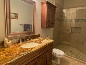 A bathroom with a marble sink, wooden cabinets, a toilet, and a glass-enclosed shower.