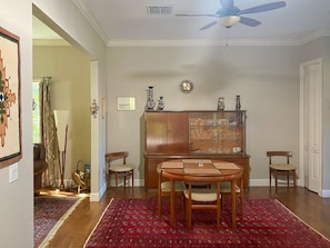A dining area with a wooden table and chairs, a red patterned rug, a wooden cabinet with glass doors, and a ceiling fan.
