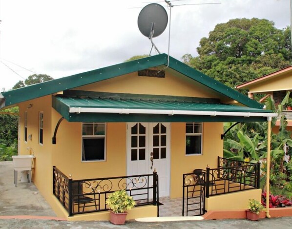 Una casa pequeña con techo verde, una antena parabólica y un balcón con barandilla metálica.