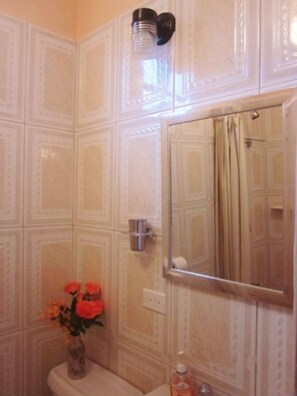 Un baño con baldosas estampadas, un espejo, un inodoro, un florero con flores y un dispensador de jabón.