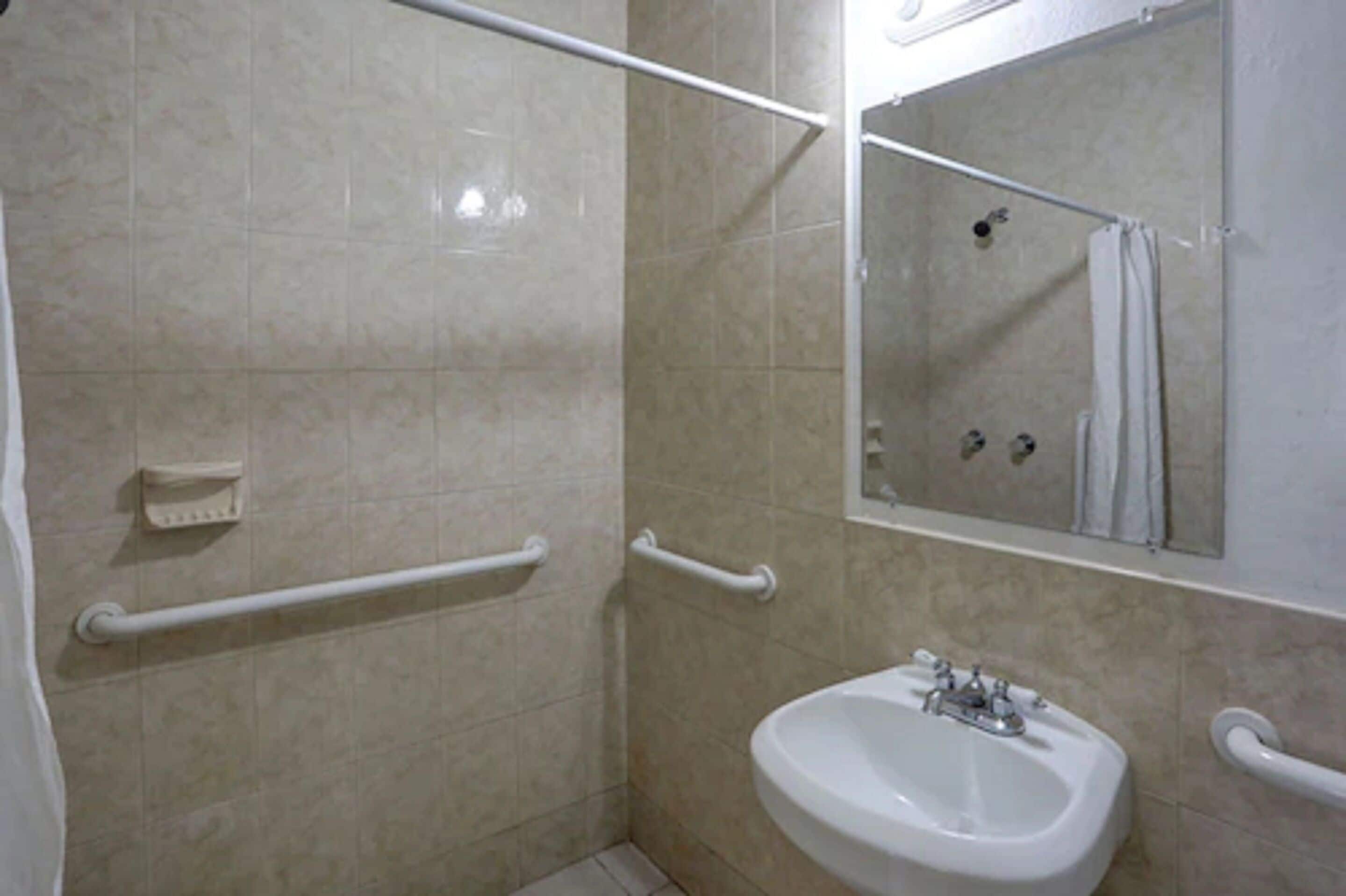Un bany amb rajoles beix, un lavabo blanc, un mirall i dues barres de sujeció.