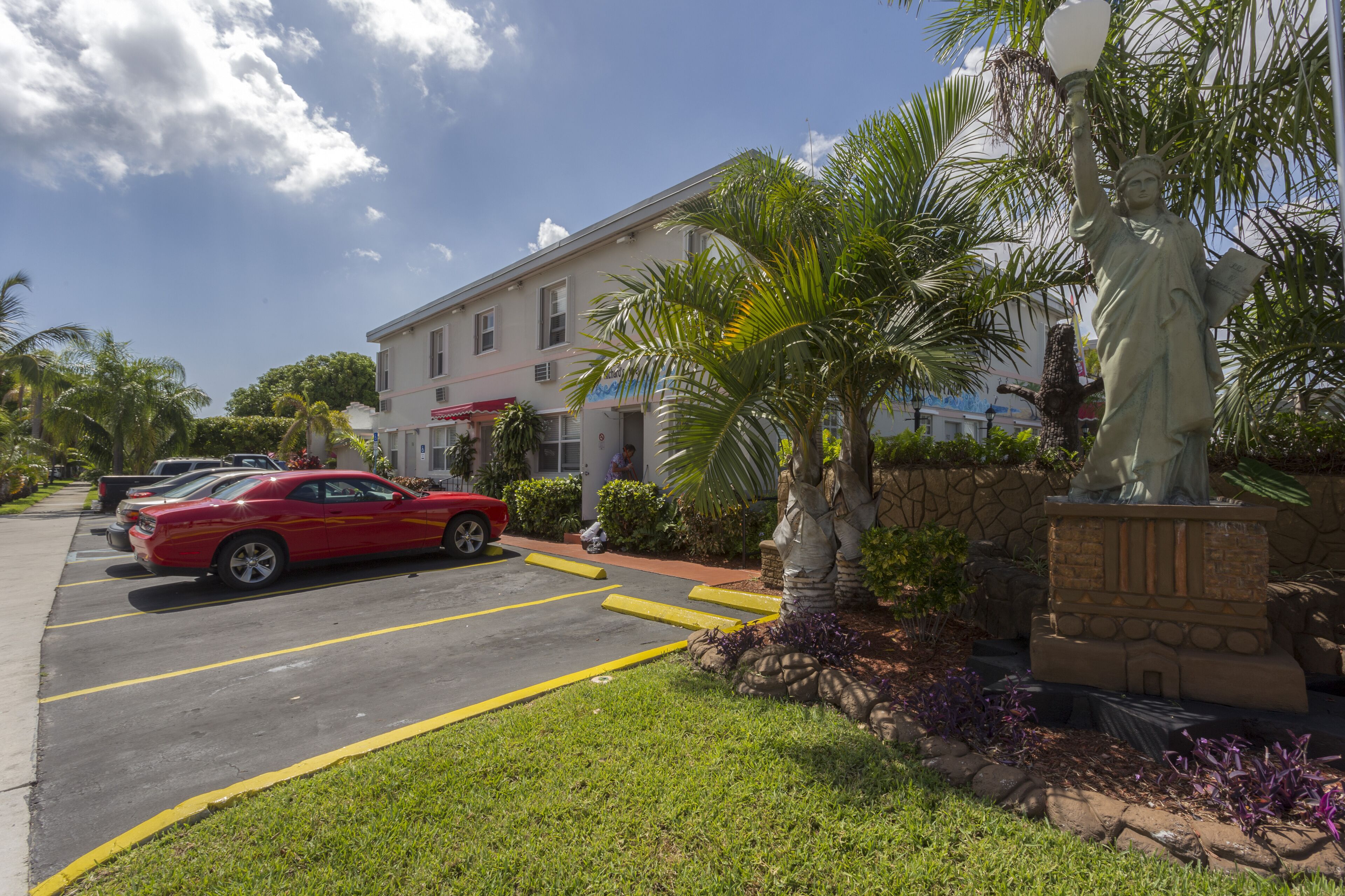 A parking lot with a statue, a building with a red awning, and palm trees.