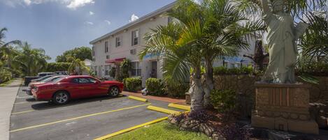 A parking lot with a statue, a building with a red awning, and palm trees.