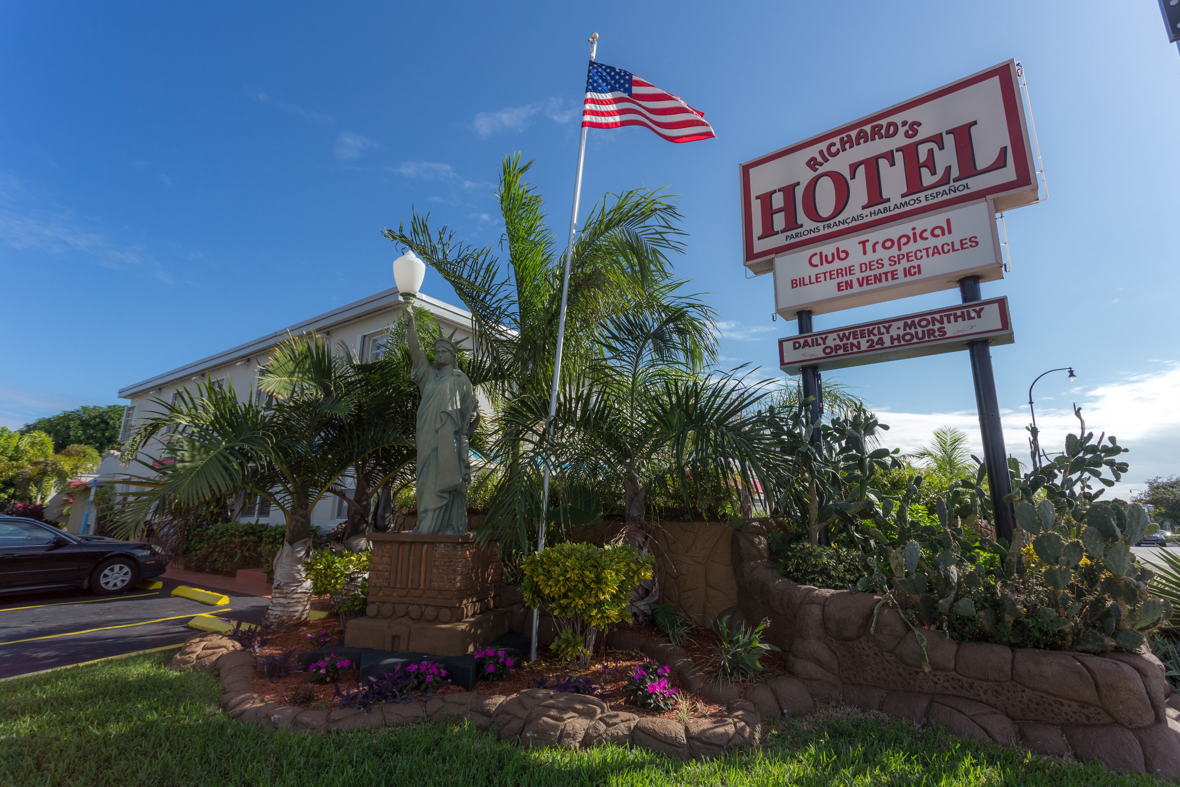 A hotel sign with "Richard's Hotel" and "Club Tropical" text, surrounded by greenery and a palm statue.