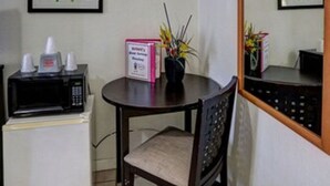 Una habitación pequeña con microondas, refrigerador, una mesa con silla y cuadros en las paredes.