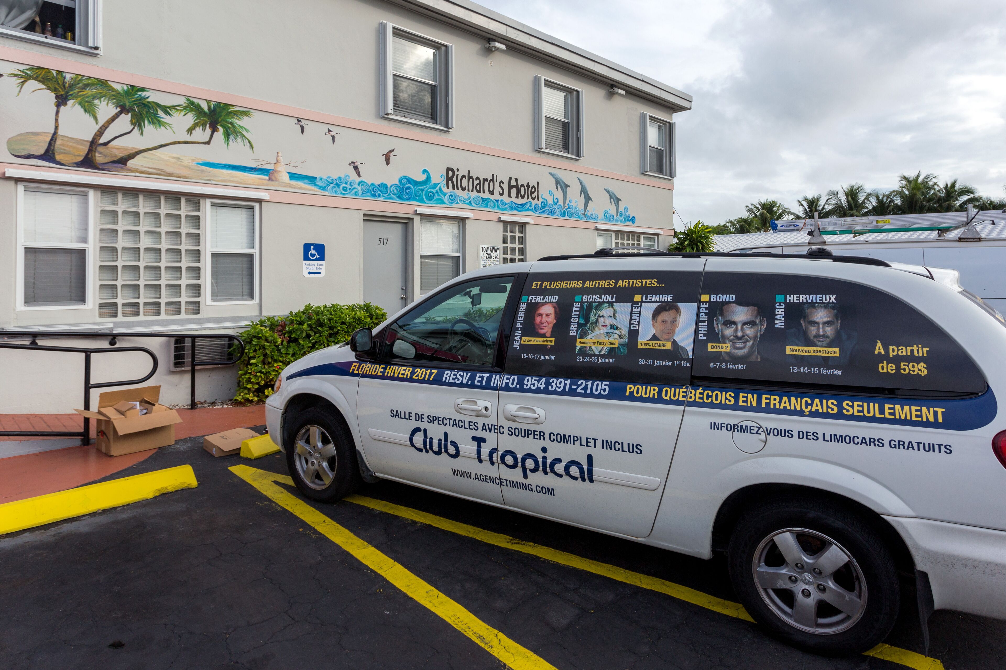 A white van parked in front of Richard's Hotel with a tropical mural on the wall.